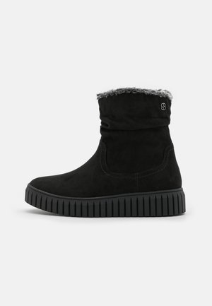 Schwarze Wildleder-Ankle-Boots mit einem umschlagbaren, flauschigen Kragen, gerippten schwarzen Sohlen und Nahtdetails an den Seiten. Seitliches Logo-Detail.
