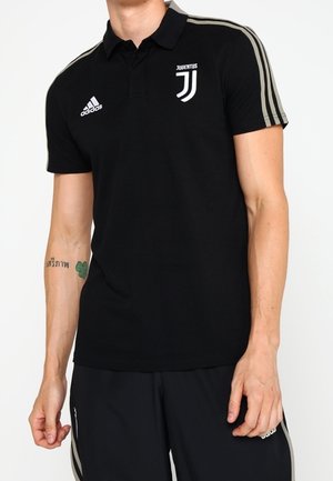 Mann trägt schwarzes Adidas Juventus Poloshirt mit grauen Streifen an den Ärmeln und passende schwarze Adidas-Hose mit grauen Streifen.