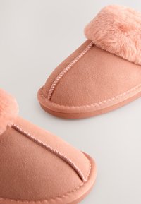 Chaussons en daim rose avec bordure en fausse fourrure, présentant des coutures contrastées, un bout arrondi et une semelle texturée pour une meilleure adhérence.