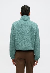 Bluza polarowa w teksturowanym miętowym kolorze z wysokim kołnierzem, ozdobiona kwiatowym wzorem, z elastycznymi mankietami i krótkim krojem.