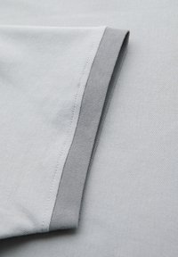 Tissu gris clair avec un bord ourlé plié pour montrer les détails de la couture sur une surface lisse et texturée.