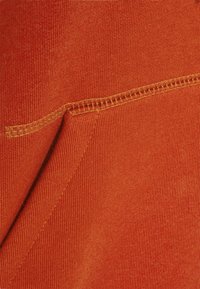 Primer plano de una tela naranja que muestra un detallado pespunte amarillo a lo largo de una costura con material doblado.