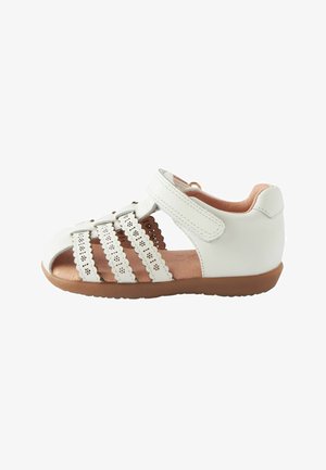 Sandale en cuir blanc avec bout ouvert, accents perforés et trois larges sangles. Fermeture velcro et semelle en caoutchouc marron. Doublure intérieure douce.