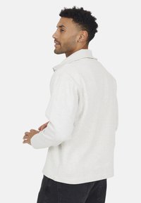 Lichtgrijze, lange mouwen pullover met kraag, vervaardigd van een textuurstof en met een ontspannen pasvorm, waarbij de achterkant zichtbaar is.