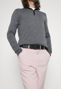 Grauer Pullover mit einem Viertel-Reißverschluss, aus gestricktem Material. Kombiniert mit hellrosa Hosen und einem schwarzen Leder-Gürtel mit silbernen Beschlägen.