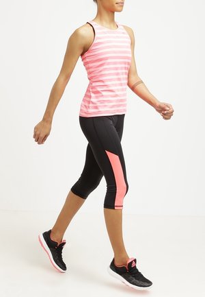 Frau geht und trägt ein pink gestreiftes Tanktop, schwarze kurze Leggings mit pinken Streifen und schwarz-pinke Sportschuhe.