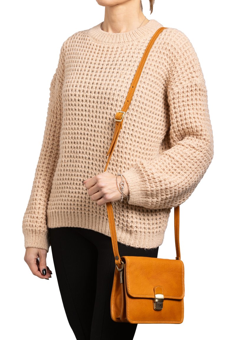 Borsa a tracolla in pelle color tan con chiusura a pattina e finiture in metallo, abbinata a un maglione di lana beige e pantaloni neri.