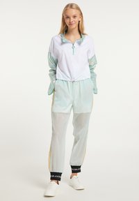 Let slim fit zip-jakke i hvid med iriserende ærmer, parret med mintgrønne bukser med elastisk talje og sorte og gyldne detaljer.