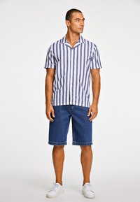 Korte mouwen overhemd met witte en marineblauwe strepen, gecombineerd met knielange denim shorts en witte sneakers. Casual zomeroutfit.