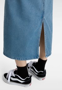 Falda de mezclilla en azul claro con detalle de abertura trasera, combinada con zapatillas negras y blancas y calcetines de canalé negros.