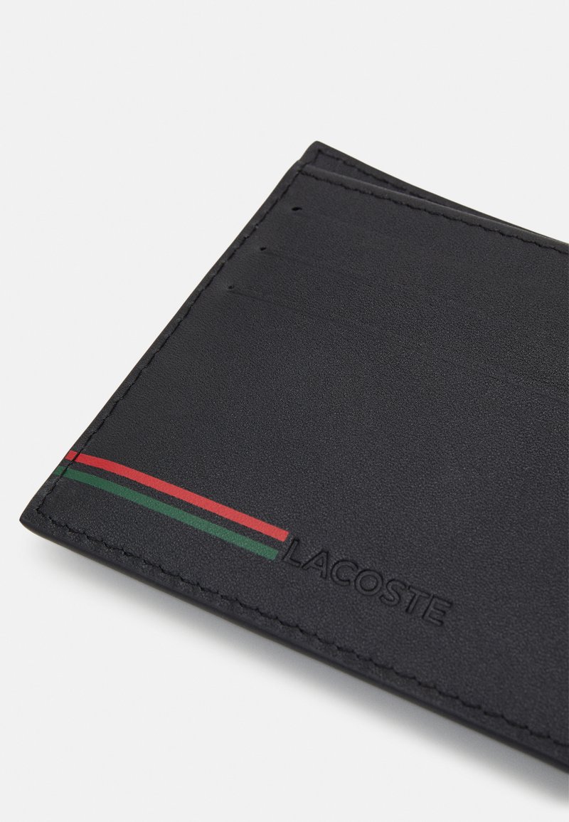 Portafoglio in pelle nera con più slot per carte, caratterizzato da un accento a strisce rosse e verdi e dalla marcatura in rilievo "LACOSTE". Texture liscia.