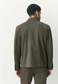 Giacca marrone con texture, dotata di colletto a punta e polsini con bottoni. Il retro presenta un design a yoke, abbinata a pantaloni coordinati.