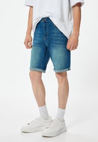 Shorts de mezclilla con un lavado azul claro a medio, dobladillo enrollado y un diseño clásico de cinco bolsillos, combinados con zapatillas blancas y calcetines tipo crew.