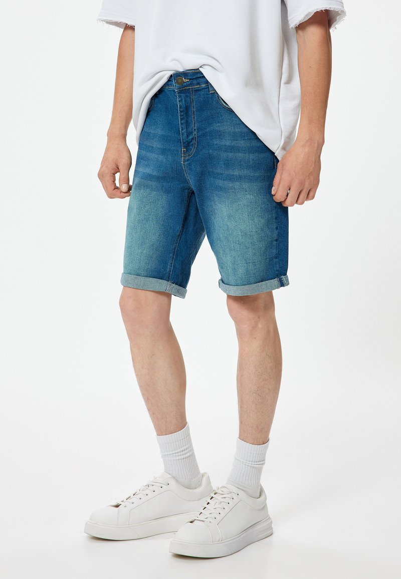 Shorts de mezclilla con un lavado azul claro a medio, dobladillo enrollado y un diseño clásico de cinco bolsillos, combinados con zapatillas blancas y calcetines tipo crew.
