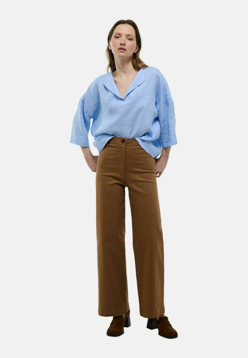 Blouse en lin bleu clair avec un décolleté en V et des manches trois-quarts, associée à un pantalon large taille haute marron et à des chaussures à talons marron foncé.
