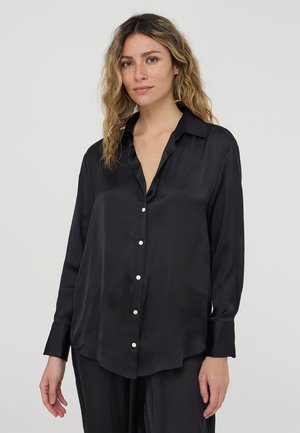 Blusa nera di seta con maniche lunghe, colletto, chiusura frontale con bottoni e orlo leggermente curvato; texture liscia e leggero splendore.