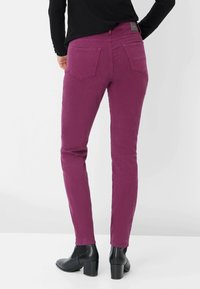 Jeans ajustados en un vibrante magenta, hechos de una tela suave con una textura lisa, que cuentan con dos bolsillos traseros y un diseño entallado. Botas negras con tacones de bloque.