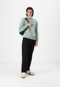 Myntegrøn sweatshirt med rund halsudskæring, sorte tapered bukser og hvide sneakers. En lille sort taske hænger over den ene skulder.
