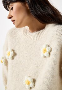 Maglione lavorato a maglia color crema con colletto a coste e decorazioni floreali tridimensionali in bianco e giallo.