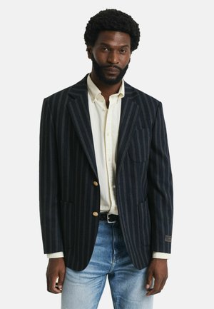 Marineblauwe gepinde blazer van wol, voorzien van twee gouden knopen, een borstzak en een comfortabele pasvorm, gecombineerd met een wit shirt en denim.