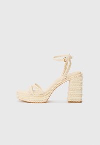 Beige hæle sandaler med remme og flettet jute platform og hæl, med en tynd ankelrem og en glat fodseng.