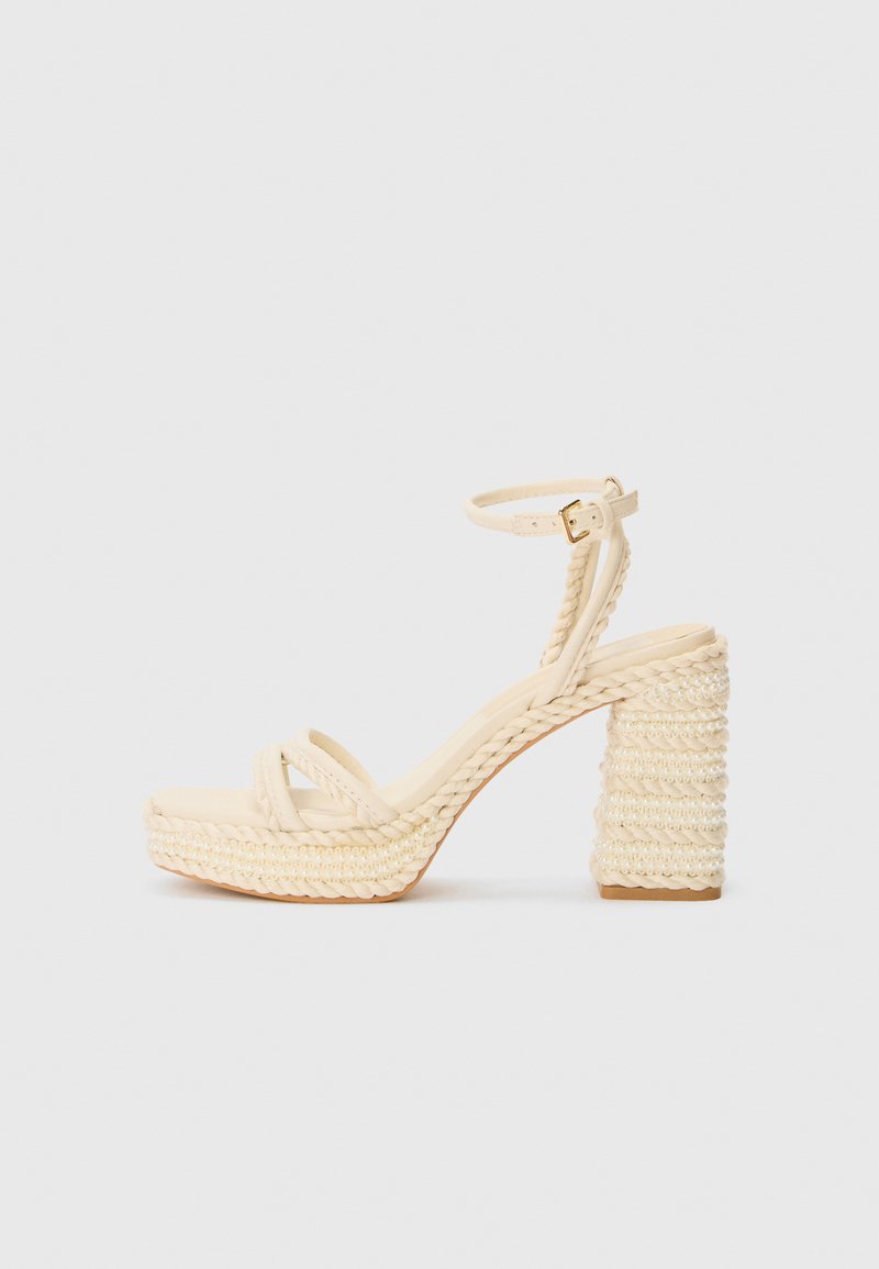Beige hæle sandaler med remme og flettet jute platform og hæl, med en tynd ankelrem og en glat fodseng.
