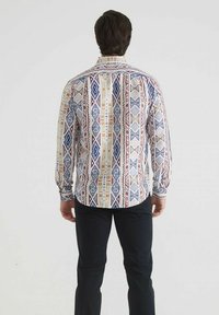 Chemise à manches longues multicolore avec des motifs géométriques, comportant des bleus, des rouges et des jaunes. Fabriquée en tissu léger avec un col standard.