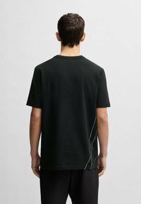 Black cotton t-shirt with short sleeves, round neckline, and a curved white stitching detail on the left side. Back view only.