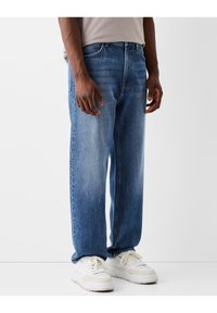 Jeans di denim azzurro chiaro con vestibilità comoda, davanti sbiadito, design a cinque tasche e cuciture a contrasto, abbinati a sneakers bianche.