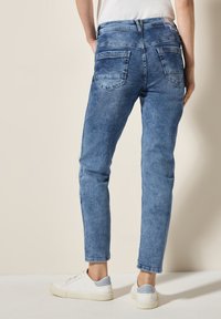Jeans in denim azzurro chiaro con vestibilità slim, dotati di vita media, due tasche posteriori e leggère scoloriture. Abbinati a scarpe da ginnastica bianche.