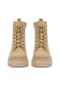 Beżowe botki za kostkę z gładkiego zamszu, z wciąganym z przodu sznurowaniem, kontrastującymi srebrnymi oczkami i masywnymi beżowymi podeszwami.