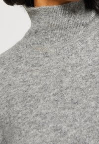 Hellgrauer Rollkragensweater mit einem gerippten Kragen und einem weichen, strukturierten Stoff, der subtile Farbvariationen aufweist.