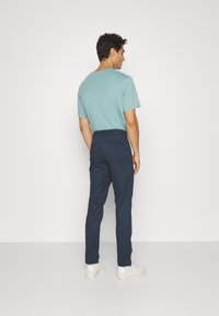 Herreoutfit med en lyseblå t-shirt og mørkeblå skræddersyede bukser med sidelommer, afsluttet med hvide sneakers.