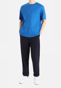 Blå kortärmad skjorta med bröstficka, i kombination med marinblå sweatpants och vita sneakers. Mjuk tygkonstruktion och avslappnad passform.