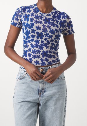 Krátký rukáv, přiléhavý top z průhledné tkaniny s modrými květinovými vzory na bílém pozadí, spárovaný se světle modrými džíny.