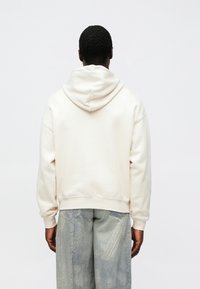 Hoodie oversized de cor creme com capuz ajustável, punhos e bainha canelados; combinado com calças texturizadas cinza claro.