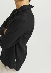 Camicia nera a maniche lunghe realizzata in un tessuto testurizzato, dotata di colletto classico, chiusura con bottoni sul davanti e orlo curvo.