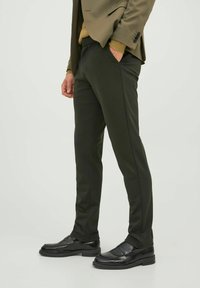 Slim-fit tmavě zelené kalhoty vyrobené z hladkého materiálu, mají boční kapsy a jemné švy, v kombinaci s černými mokasínami.