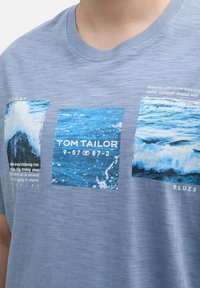 Niebieska koszulka z miękkiej bawełny z trzema nadrukami zdjęć oceanicznych fal i detalami tekstowymi, z okrągłym dekoltem i krótkimi rękawami.