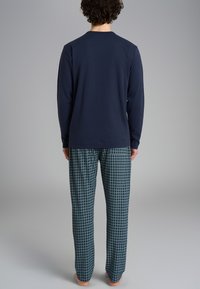 Maglietta a maniche lunghe blu navy abbinata a pantaloni verdi a scacchi con motivo a quadretti e tasche laterali, realizzati in tessuto morbido, vestibilità casual.