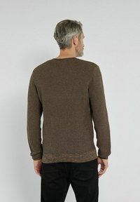Brązowy sweter z dzianiny z teksturowanym wzorem, okrągłym dekoltem i długimi rękawami, zestawiony z czarnymi spodniami. Pokazany widok z tyłu.