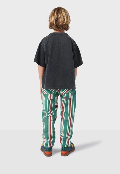 Zwarte katoenen t-shirt met korte mouwen, gecombineerd met groene gestreepte broeken met rode en witte lijnen. Bruine schoenen met kleurrijke accenten.