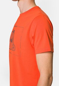 Pomarańczowa bawełniana koszulka z grafiką roweru. Krótkie rękawy, okrągły dekolt, gładka faktura i prosty krój.