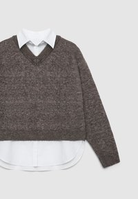 Pullover a maglia marrone con scollo a V, caratterizzato da una finitura texturizzata, indossato sopra una camicia bianca con colletto, orlo curvato e dettagli con bottoni.