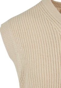Kremowy, bezrękawnik z dzianiny o prążkowanej fakturze, z dekoltem w kształcie litery V i gładkim wykończeniem brzegów.