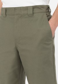 Pantaloni verde oliva realizzati in un tessuto resistente presentano una vestibilità dritta, tasche frontali e una texture liscia con dettagli di cucitura puliti.