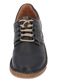 Zapato de cuero negro con cordones beige, acentos de costura, punta redondeada y suela marrón texturizada. El interior presenta un material con apariencia natural.