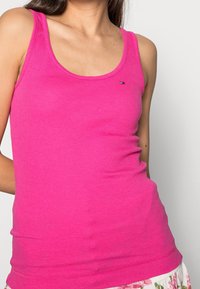 Top de tirantes sin mangas en color rosa con un diseño ajustado, hecho de tela acanalada, que presenta un pequeño acento de logo. Textura suave y escote redondo.