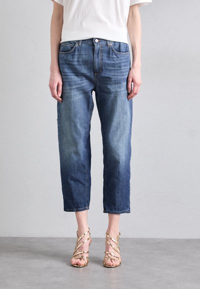 Pantalones de mezclilla en azul claro con un ajuste relajado, cortos a la altura del tobillo, con un lavado desgastado y diseño de cinco bolsillos. Combinados con sandalias metálicas.