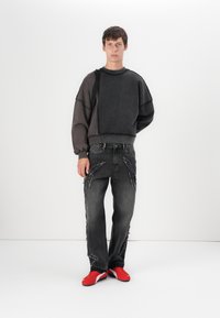 Sudadera negra de gran tamaño con dobladillo deshilachado, combinada con jeans negros desgastados que presentan acentos deshilachados y zapatillas deportivas rojas.